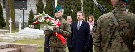 żłonierz trzyma patriotyczną wiązankę, za chwilę położy ją na pomniku, za nim stoi Paweł Wojciechowski Zastępca Burmistrza Miasta Hrubieszowa.