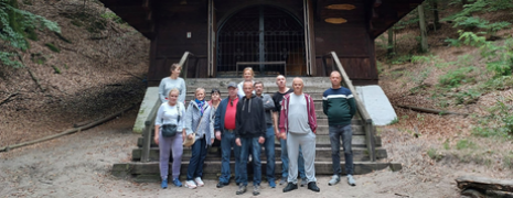Grupa osób stoi na tle drewnianej kaplicy