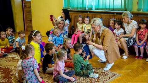 Marta Majewska burmistrz miasta, częstuje dzieci siedzące w sali na dywanie  lizakami