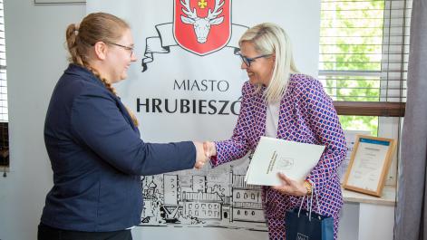 Marta Majewska trzyma w ręku teczkę z herbem miasta, gratuluje uśmiechniętej zawodniczce