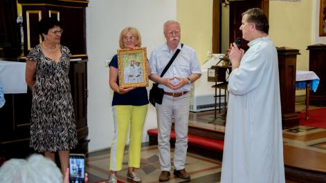 Seniorzy z Krakowa trzymają w rękach ikonę Matki Bożej, obok stoi Gwardian, coś do nich mówi przez mikrofon