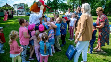 Dzieci przytulają Hrubcia Burmisztrz stoi obok, trzyma w ręku torbę z lizakami