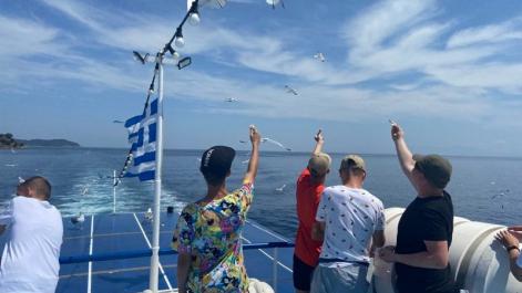 Młodzież płynie statkiem, na maszcie powiewa flaga grecji