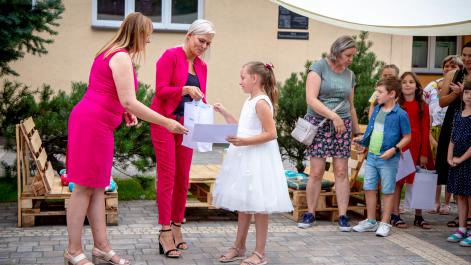 Prezes gratuluje dziewczynce nagrody obok burmistrz miasta trzyma prezent dla dziewczynki