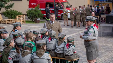 Harcerze siedzą na widowni, w tle dorośli przygotowują się do występu